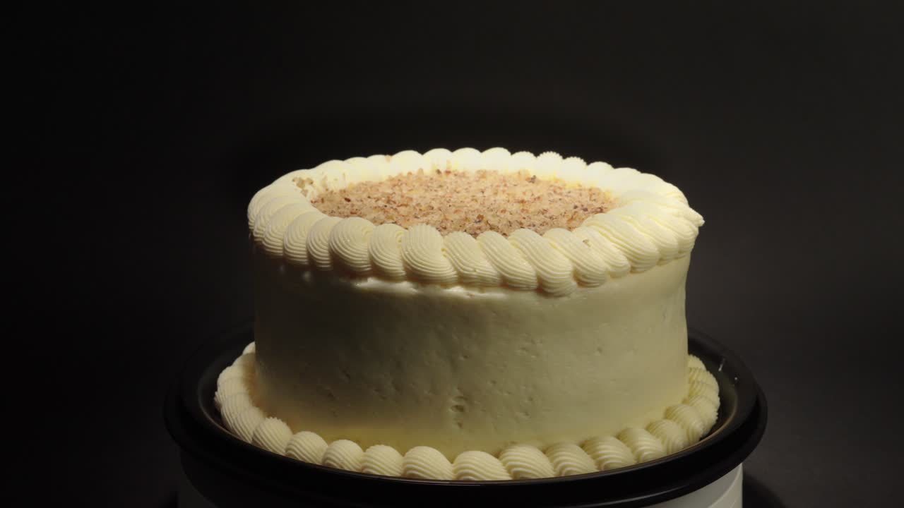 Torta di carote con copertura di crema e noci, isolata su un piatto girevole con sfondo nero, un dolce vegetale delizioso e salutare.