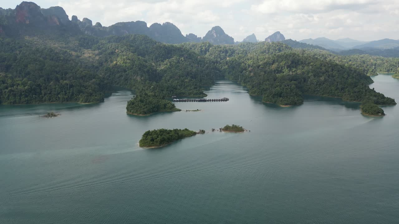 Ampia ripresa aerea di un drone che sorvola in avanti il lago Cheow Lan verso bungalow galleggianti. Acqua turchese e montagne calcaree nel parco nazionale di Khao Sok, Thailandia. Qualità 4K