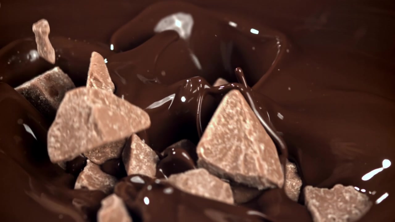 Chokoladestykker falder ned i smeltet chokolade i slowmotion