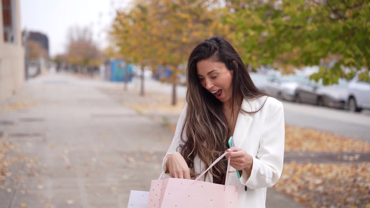 Una giovane donna elegante tiene gioiosamente borse della spesa in un vivace contesto urbano autunnale.