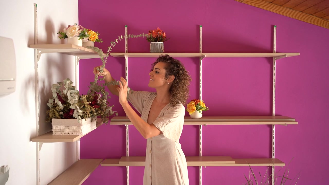 Una donna decora gli scaffali del soggiorno di casa sua con decorazioni floreali.