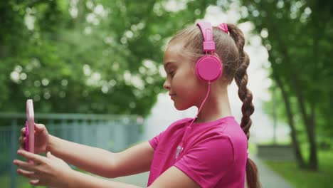 a young girl enjoys music while taking a selfie in a lush green park with vibrant atmosphere, signifying joy and the connection of technology with nature