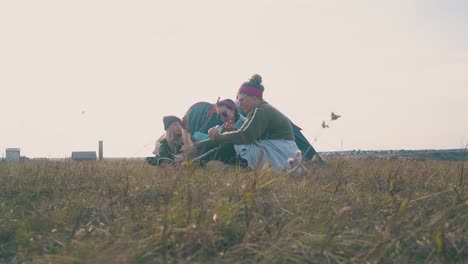 happy-girls-rest-sitting-on-grass-at-blue-tent-in-evening