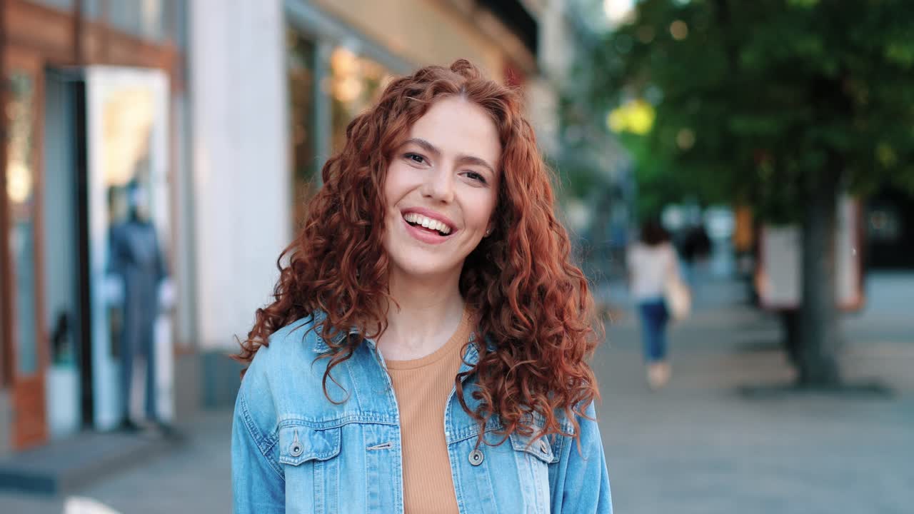 vista trasera de una mujer pelirroja caminando por la calle, luego se vuelve y mira la cámara