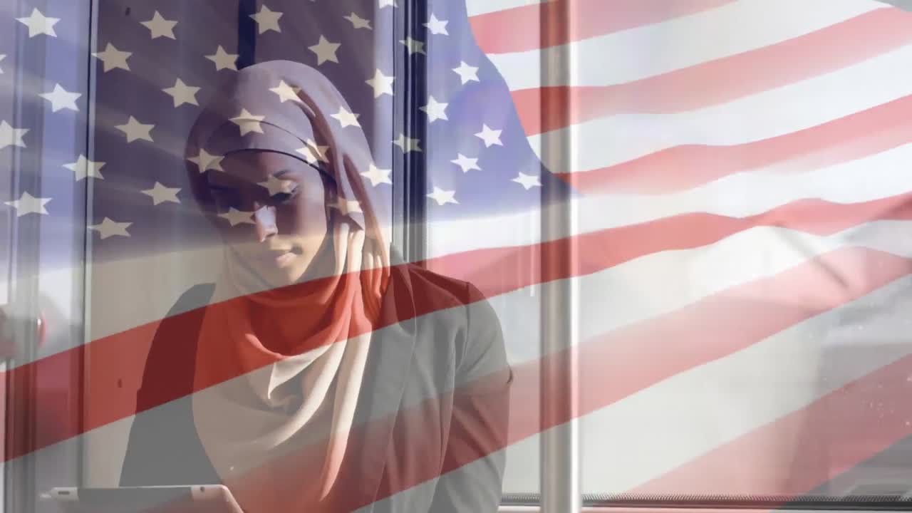 animación de la bandera estadounidense ondeando sobre una mujer de raza mixta en hijab usando una tableta digital