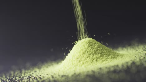 Video-of-close-up-of-green-sand-grains-pouring-into-heap-and-copy-space-on-black-background