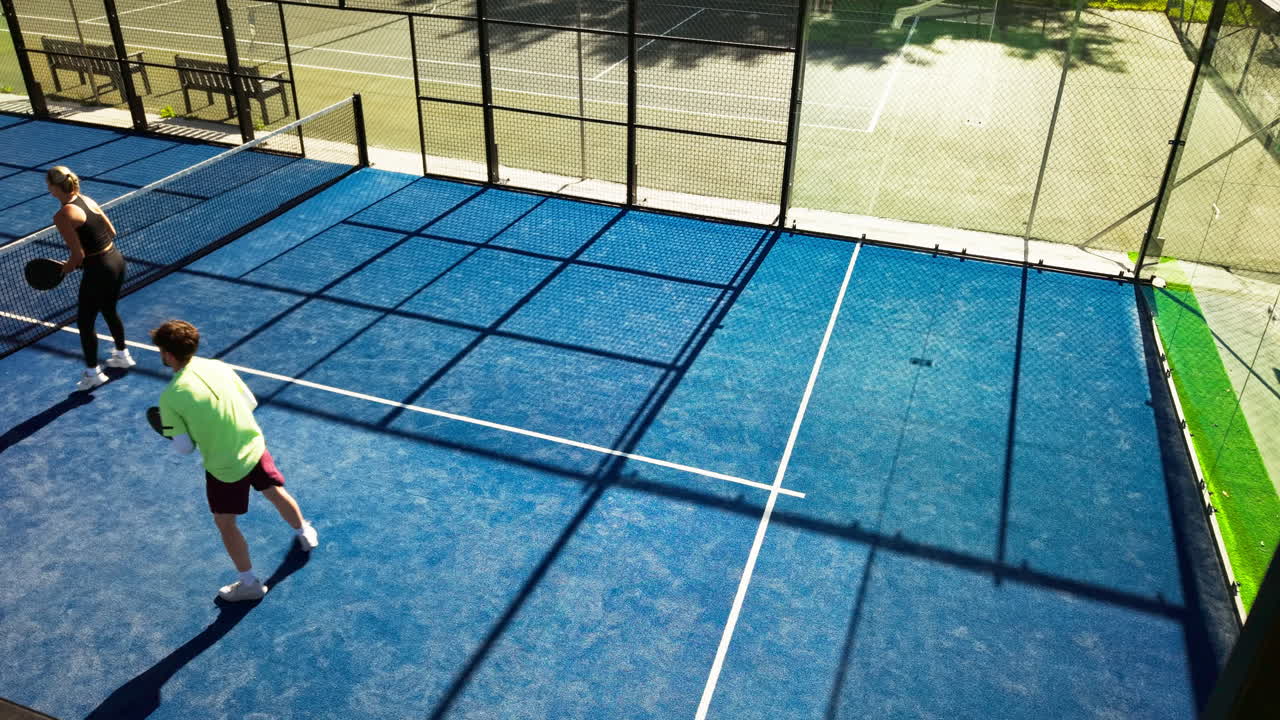Aufnahme aus der Vogelperspektive von zwei Personen, die Padel-Tennis auf einem blauen Spielfeld spielen