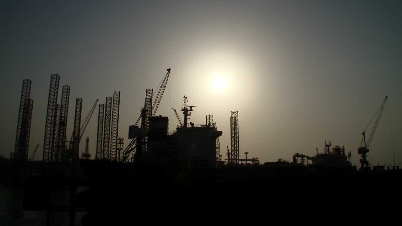 Panorering ned på silhuet af olieboreplatforme i havn, der afventer reparationer og vedligeholdelse på tørdokken i Bahrain