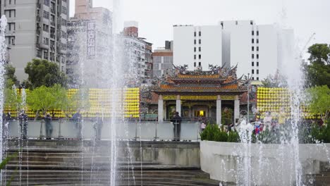 exterior of lungshan temple viewed from bangka park with rising water fountains in the foreground, taipei city, taiwan