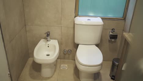 a slow-moving shot captures a hotel bathroom featuring both a bidet and a normal toilet, highlighting the clean, elegant design and upscale amenities for a luxurious guest experience