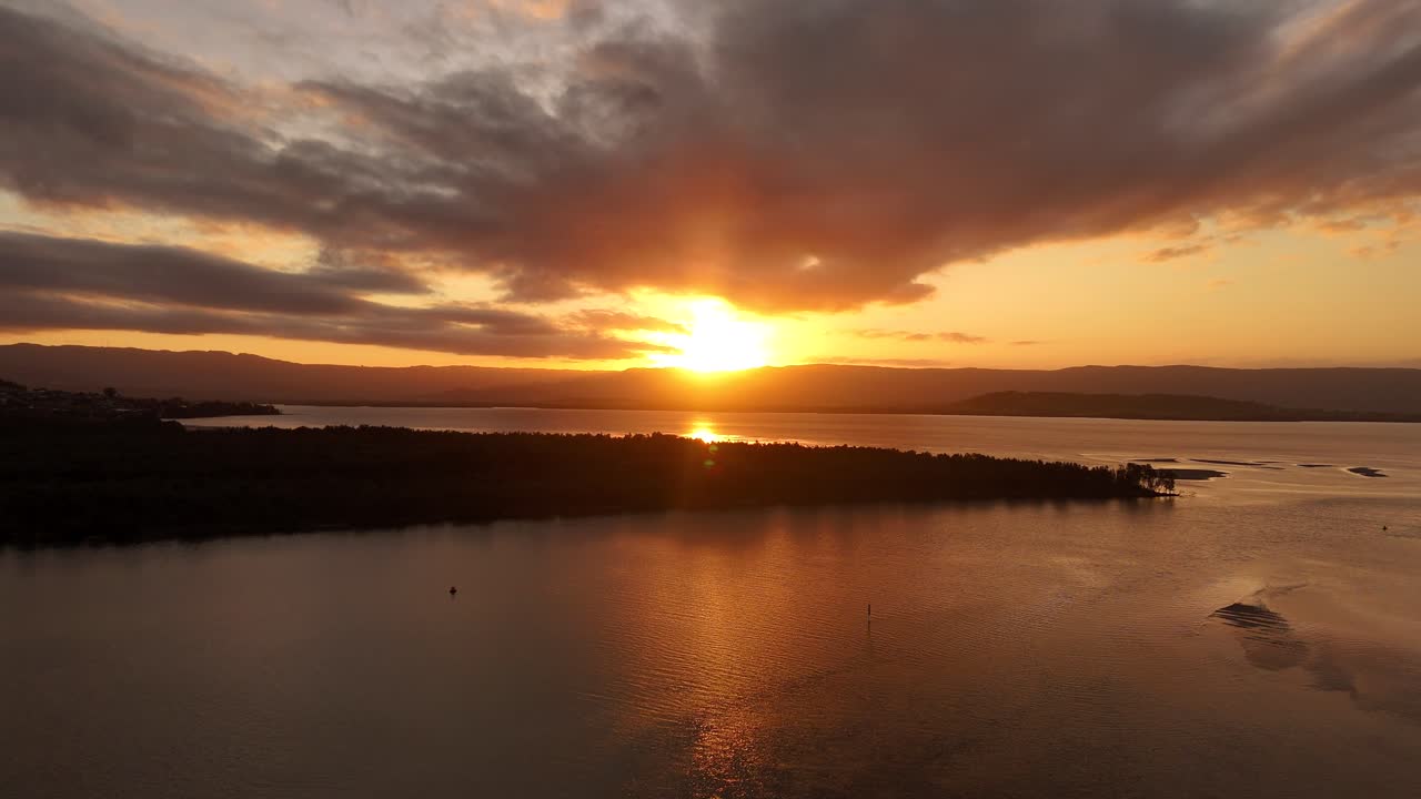Vibrant sunset colors over Lake Illawarra with the water reflecting the golden hour sky in Australia, aerial dolly over homes