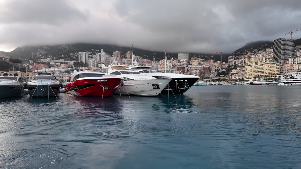 La Condamine, Monaco - 4 luglio 2025: fila di yacht di lusso ormeggiati a Port Hercules, con il paesaggio urbano di Monaco e le colline nebbiose sullo sfondo