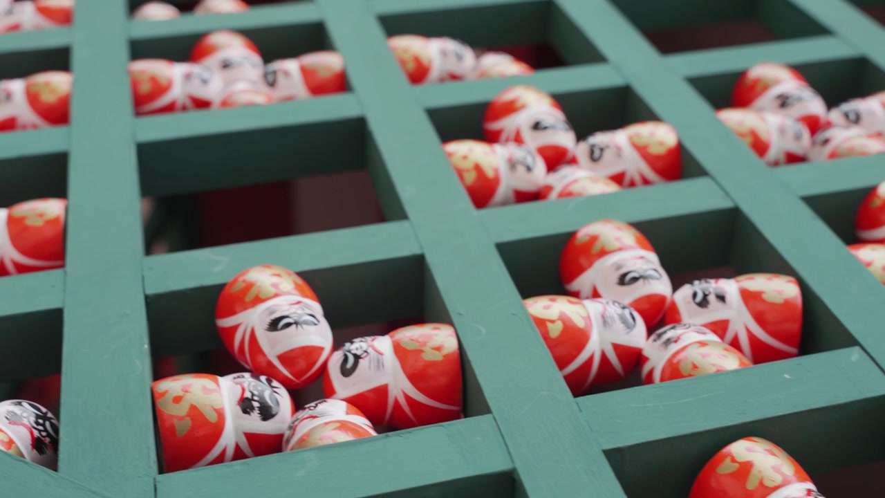 Traditional Daruma dolls line wooden green shelves at Katsuoji Temple in Osaka, offering visitors a colorful glimpse into Japanese culture, spirituality, and beliefs surrounding good fortune.