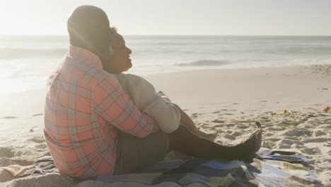 una pareja afroamericana de alto nivel sonriente abrazándose y sentada en una playa soleada