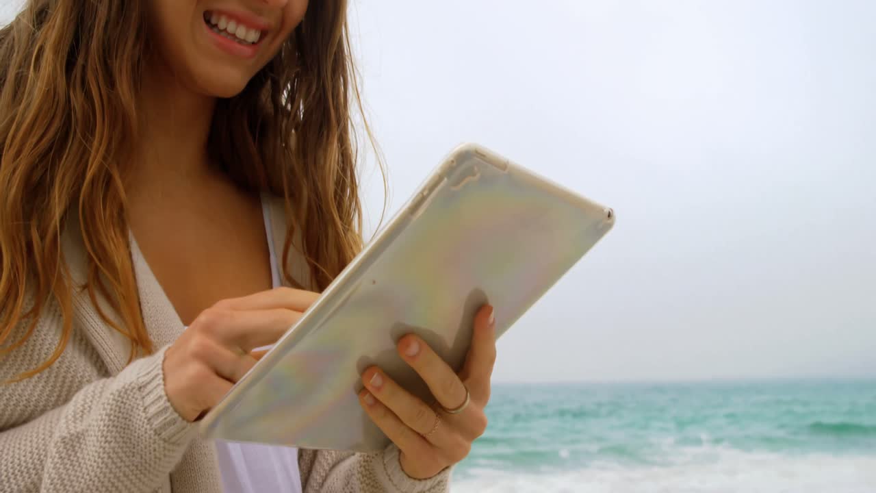 vista frontal de una mujer caucásica usando una tableta digital en la playa 4k