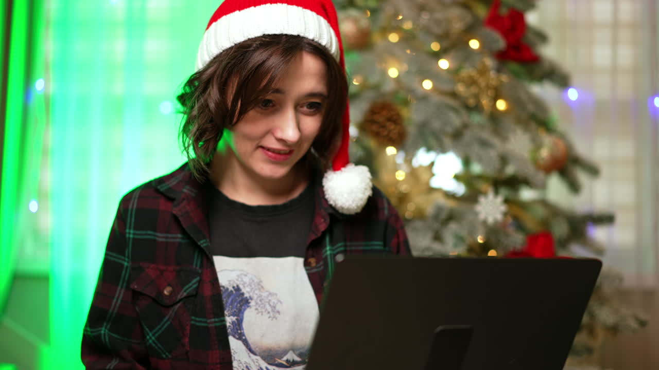 Joyful Christmas celebrations!. A person wearing a Santa hat smiles while sitting in front of a decorated Christmas tree, sharing holiday cheer