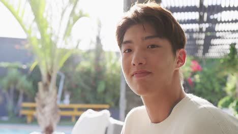 portrait of happy asian male teenager sitting and relaxing on sunny day in garden