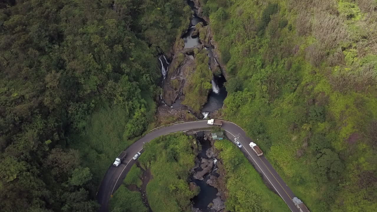 Slowly spiraling above a stream of vehicles on a Hana Highway bridge, Hanawi Falls, aerial god view