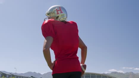 american football player standing with helmet and rugby ball