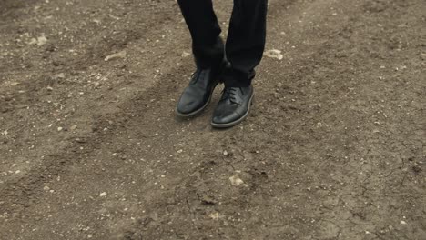 un hombre vestido con una camiseta blanca y pantalones oscuros se pasea por un camino de tierra rodeado de extensos campos verdes