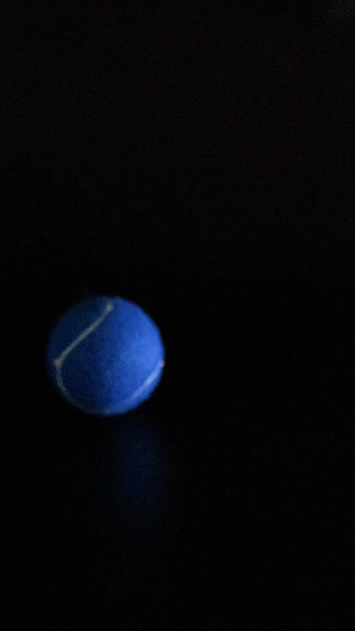 A vibrant blue tennis ball bounces and moves through a dark, minimalist vertical frame.