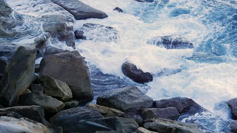 shoreline of rocky hills with waves crashing over stones and rocks