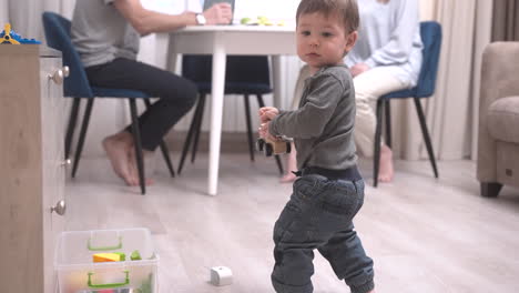 parents sitting at a table while their baby is sitting on the floor playing with toys