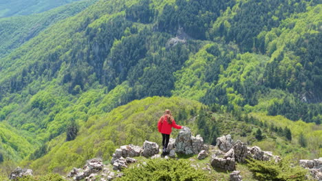 a solo female hiker enjoys a panoramic view over meadows, forests, and rolling hills at beklemeto pass, bulgaria. the perfect scene of peace, freedom, and adventure in nature during springtime.