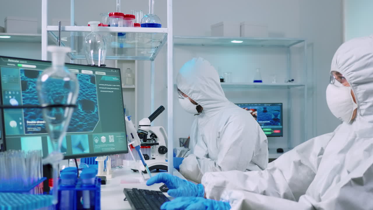 médico en traje de ppe trabajando en la pc mientras el químico usando el microscopio