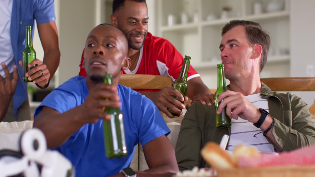 Amici di diverse etnie che guardano un uomo con una maglietta blu prendere una bottiglia verde, festeggiando una partita con la VR.