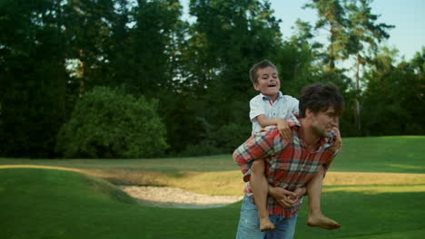 Padre-E-Hijo-Jugando-Juntos-En-El-Parque.-Hombre-Corriendo-En-Campo-Verde-Con-Niño