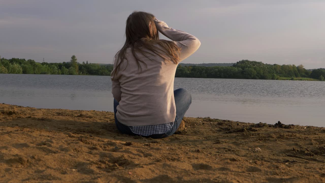 Solitary woman relaxing by lakeside looking into the distance wide shot