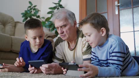family using technologies at home. happy old man and his grandchildren relaxing on the floor at home while playing mobile phone together