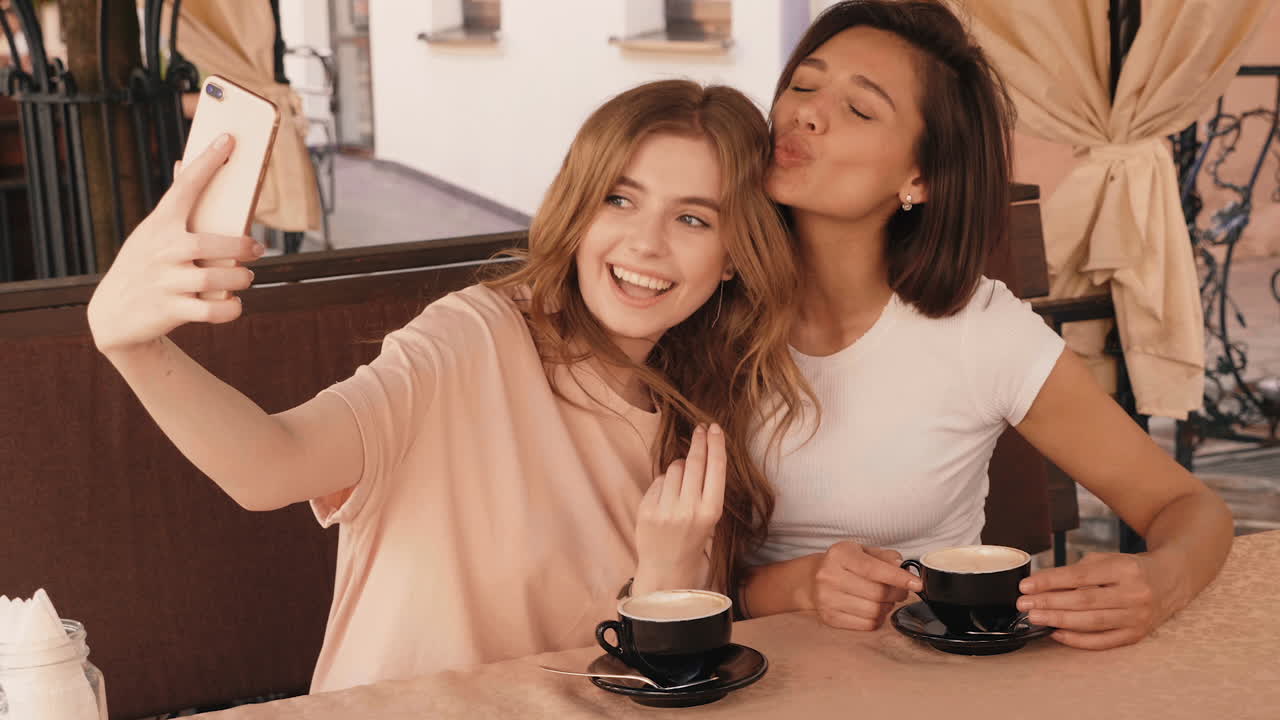 두 친구가 카페에서 셀피를 찍고 있다