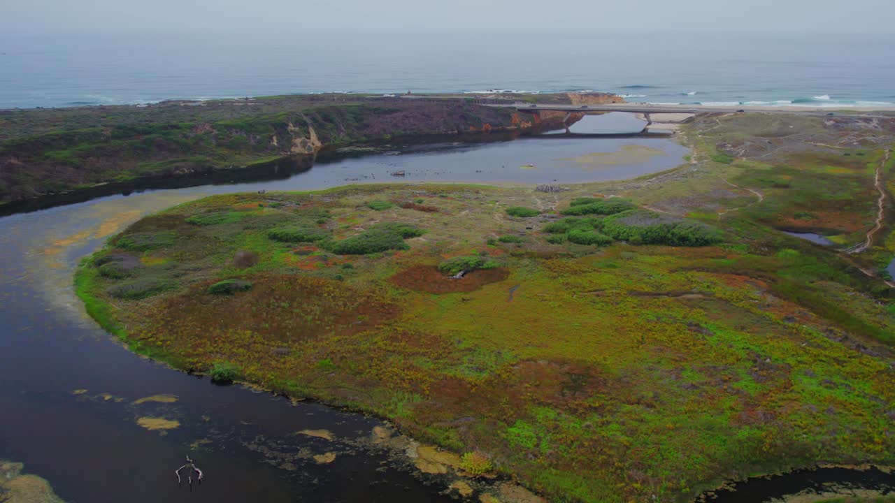 tiro de dron giratorio de una laguna sinuosa que conecta con el mar y revela un puente con camiones cruzando en el fondo
