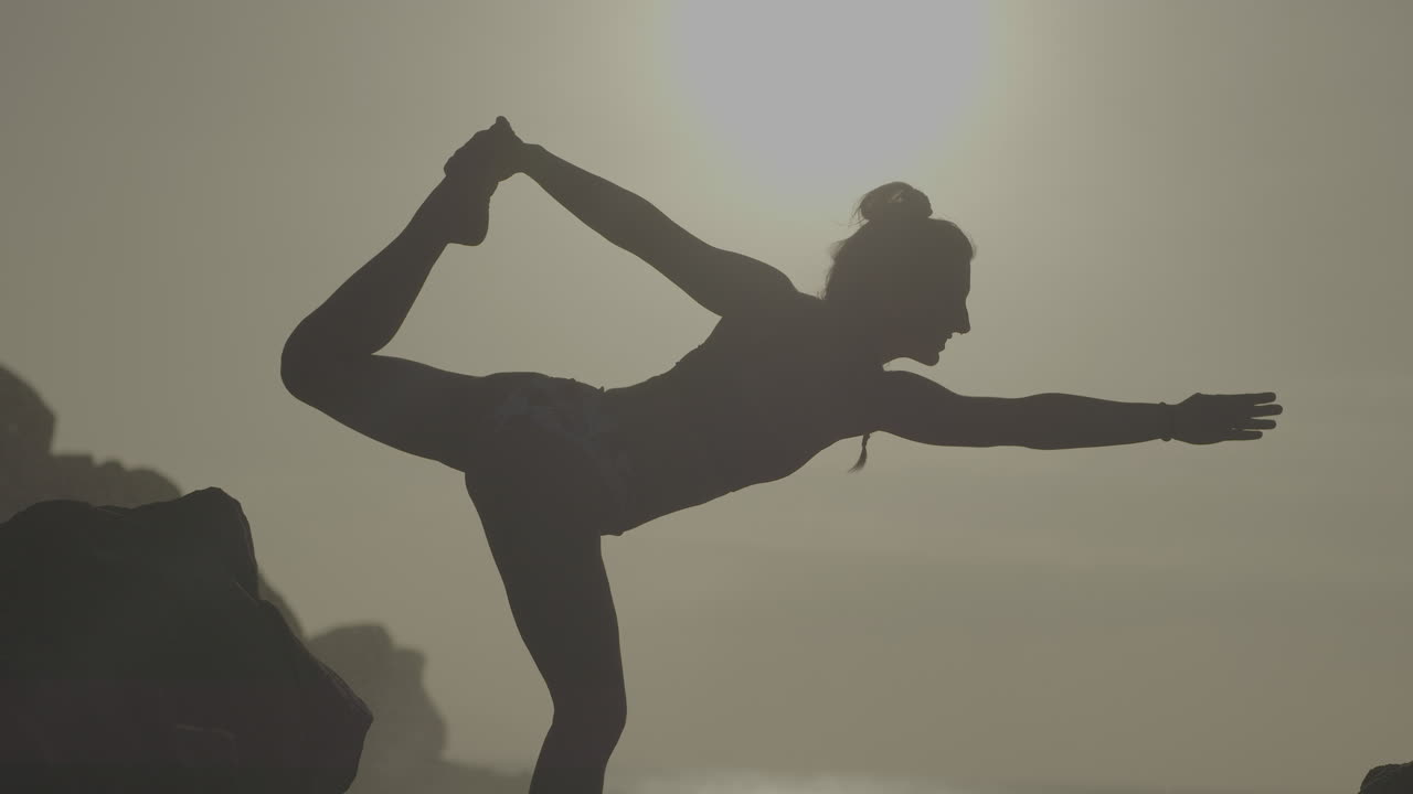 Woman practicing yoga on a rocky beach at sunset