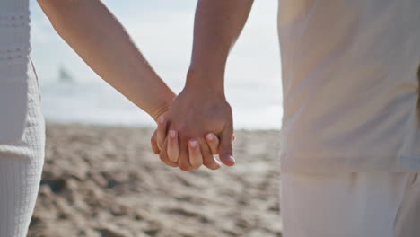 pregnant couple holding hands walking beach closeup. expecting pair strolling