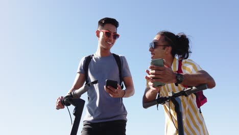 Happy-diverse-gay-male-couple-using-smartphones-at-promenade-by-the-sea,-slow-motion