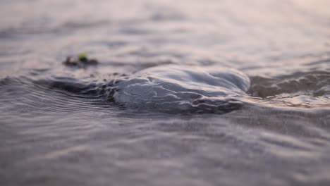 slow motion of a small wave hitting a rock on the beach with a beautiful sunset