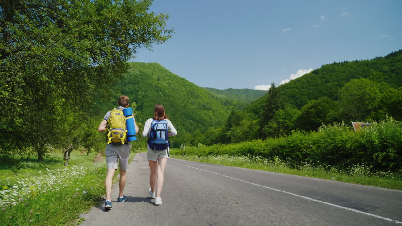 배낭을 메고 있는 두 명의 관광객이 아름다운 녹색 m을 향해 아스팔트 도로를 따라 걷고 있다
