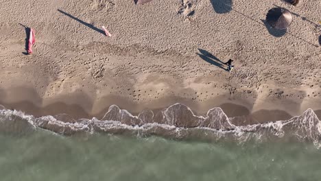 Areal-shot-of-couple-walking-on-a-sandy-beach-near-the-sea-during-sunset