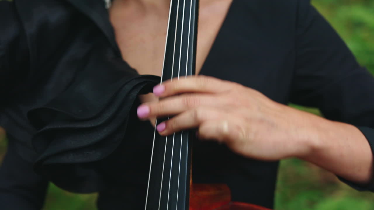Cello playing. Woman's fingers perform music on strings of a cello. Musical instrument in female's hands outdoors. Close-up.