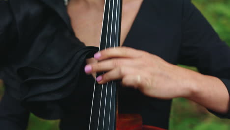 cello playing. woman's fingers perform music on strings of a cello. musical instrument in female's hands outdoors. close-up.