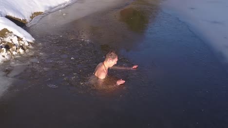 young man under water in partially frozen mountain lake rises to the surface and turns to exit