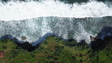 Toma-Aérea-De-Drones-De-Olas-Que-Golpean-El-Acantilado-Con-árboles-Verdes-Demasiado-Grandes