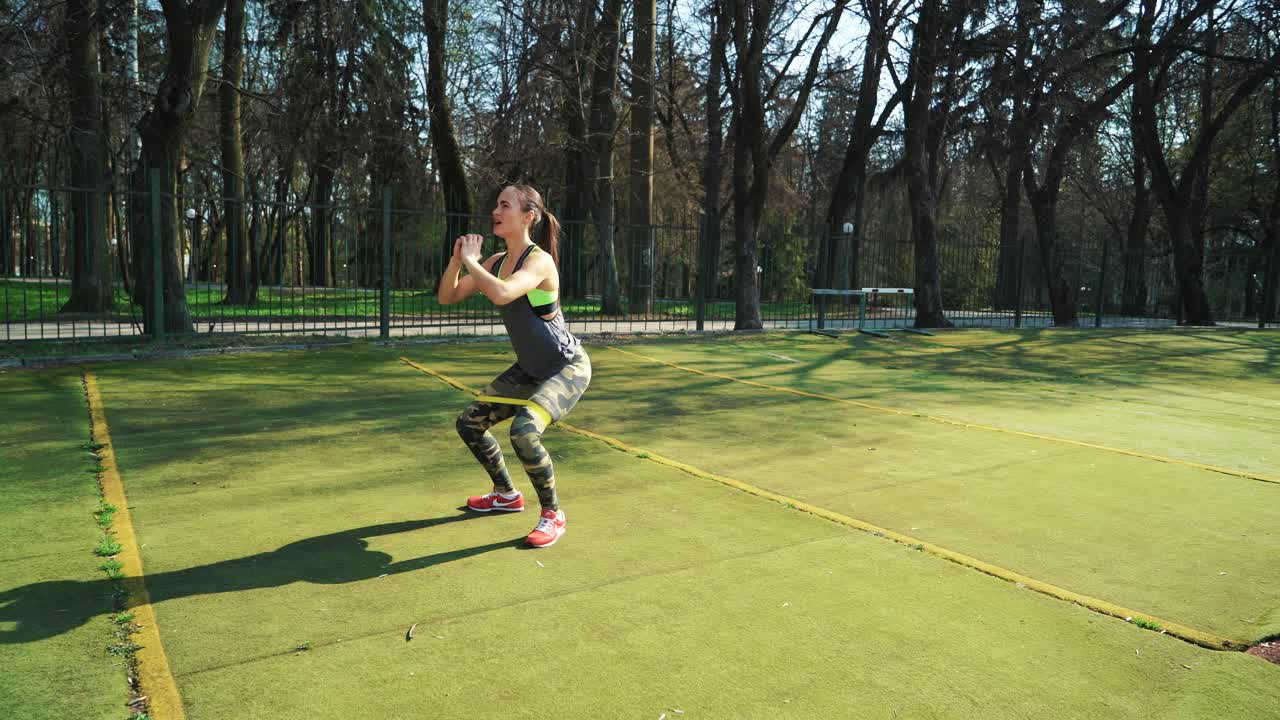 Woman doing exercises outdoors at the stadium. Beautiful young woman working with elastic band. Fitness concept.