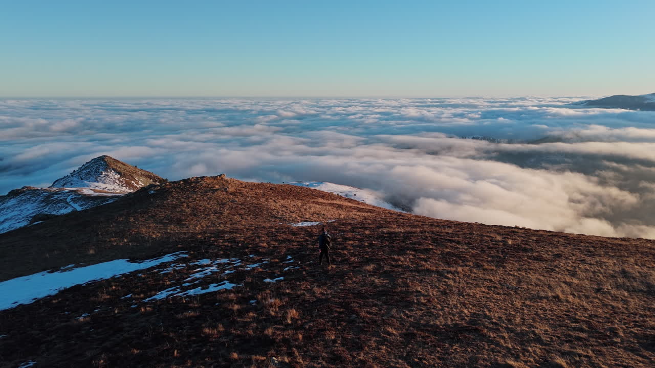 Person on mountain summit above clouds at sunrise, feeling freedom