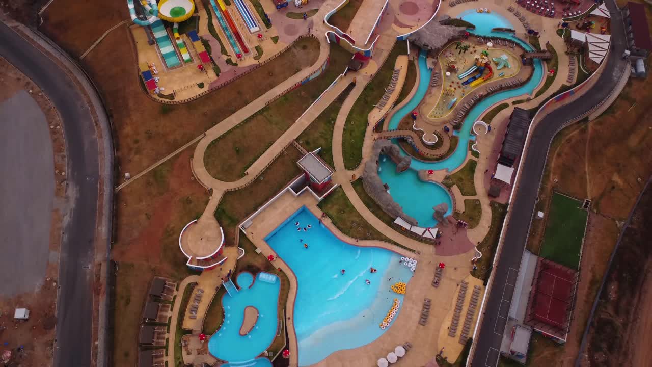 Aerial view of a newly developed waterpark in Abuja, Nigeria. The drone slowly ascends and reveals the full park with slides and a variety of pools at the tourist attraction