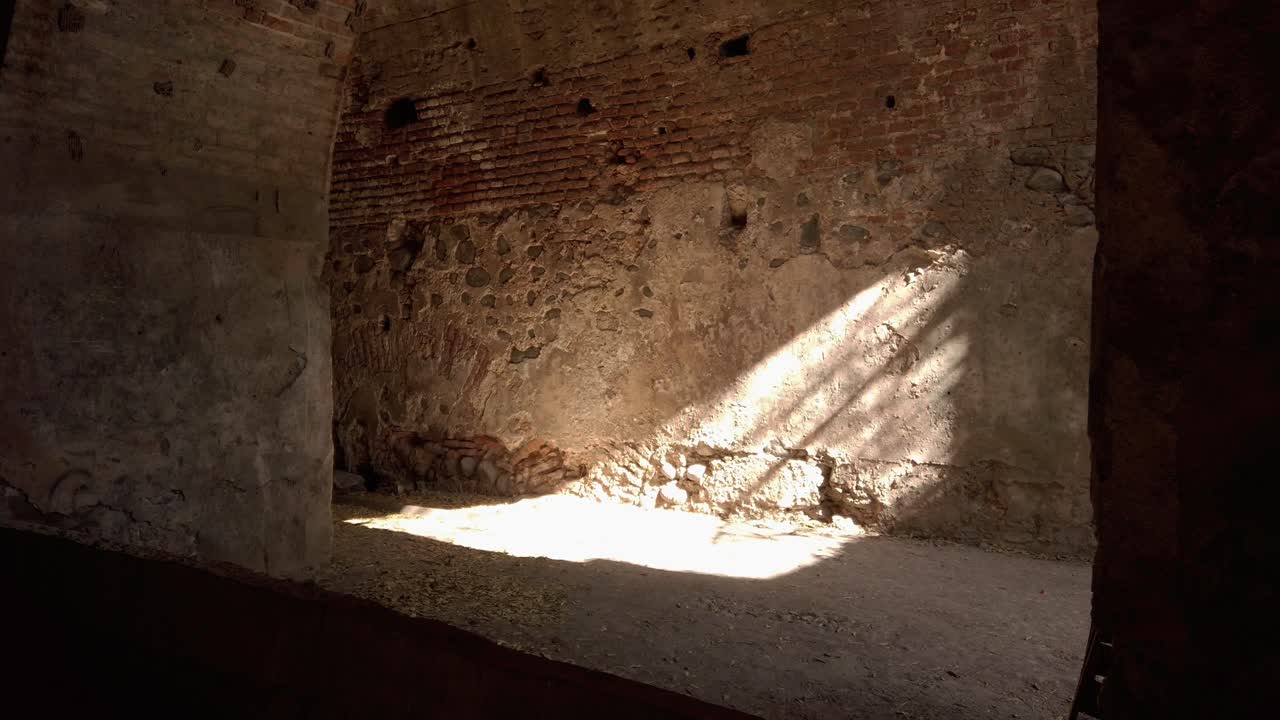 Vista interna di un'hacienda abbandonata con pareti dalla texture grezza e un forte raggio di sole che crea contrasti e ombre su una superficie invecchiata in uno spazio storico e tranquillo