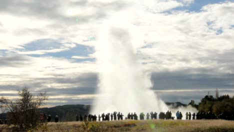 eruption of strokkur geyser, view from distance from backs of tourists, in sunny daytime in a fall